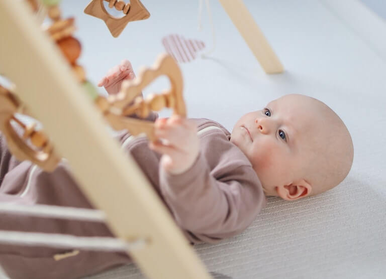 Baby under wooden mobile smiling