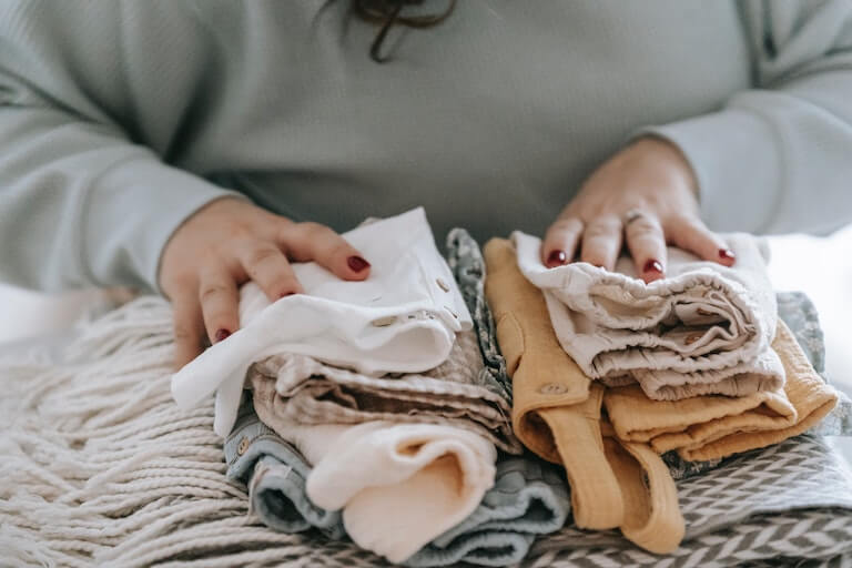 Mom sorting baby clothes on a bed