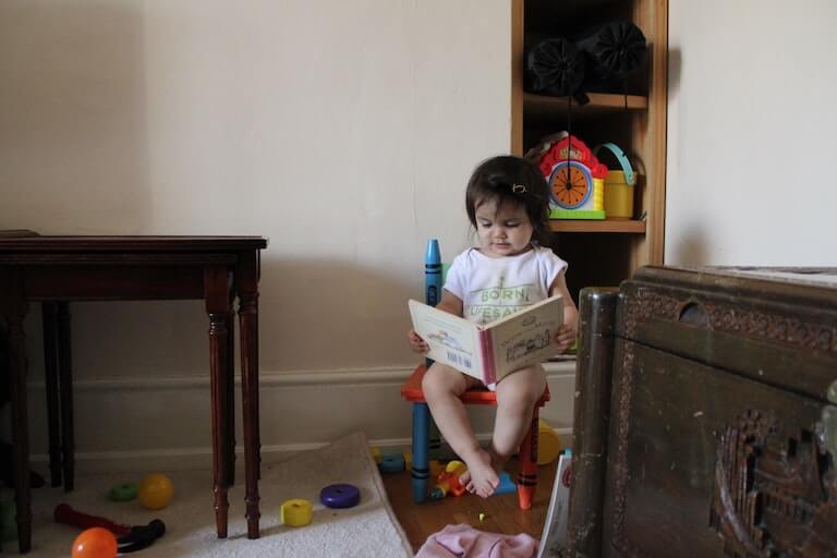 Little girl sitting on a chair and reading a book