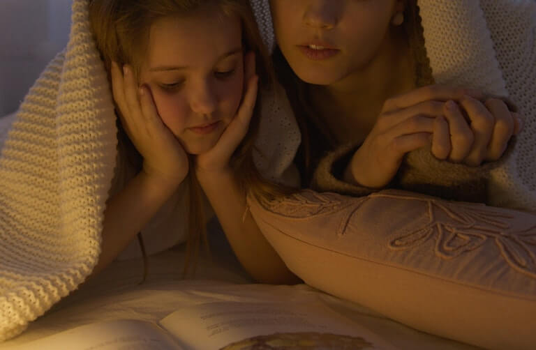 A mom and daughter reading a book under a blanket