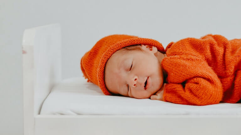 Baby in orange outfit sleeping on their side
