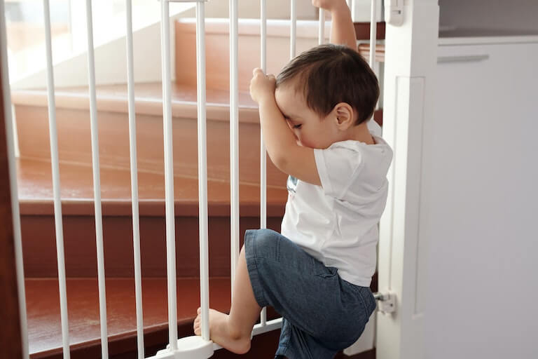 Baby at the bottom of the stairs behind a gate