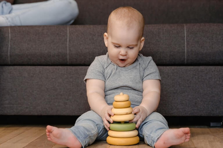 Little boy sitting on the ground and playing with a wooden toy