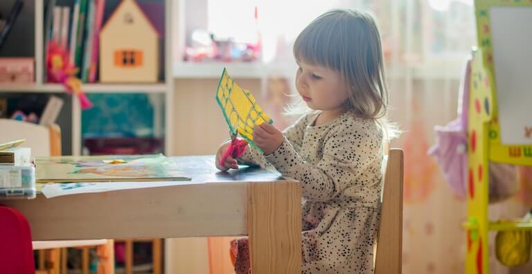 Little girl cutting paper doing arts and crafts in kindergarten