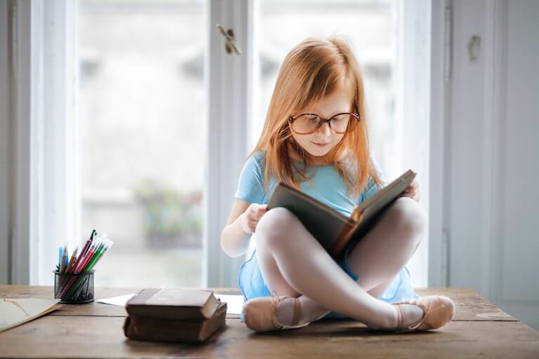 Little girl sitting down reading a book at home