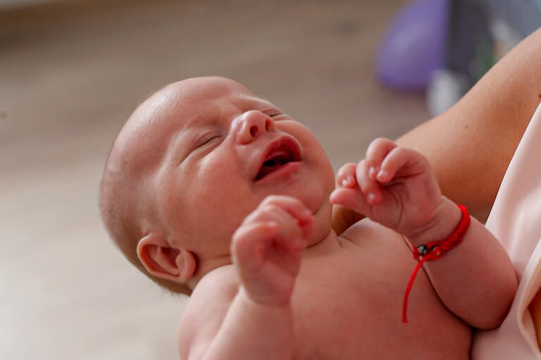 A baby crying with their mouth open and gums showing