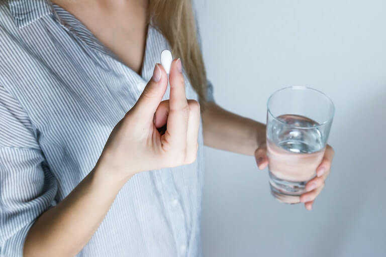 Woman with a pill in one hand and a glass of water in the other hand
