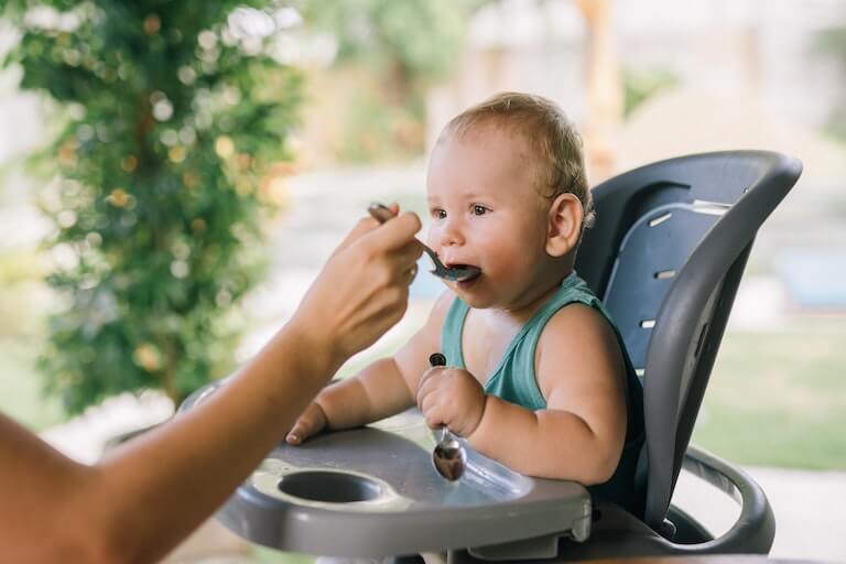 Baby in a chair eating food off a spoon