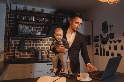 Father working at a laptop while holding his young son