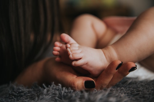 Mother holding baby feet alone in bed