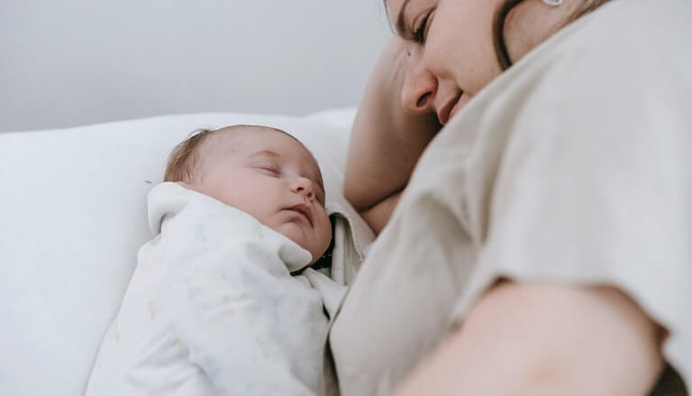 Swaddled baby sleeping next to mother
