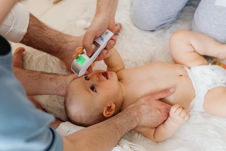 Baby in a diaper getting their temperature taken