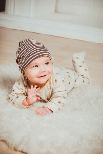 A baby laying on their stomach and waving